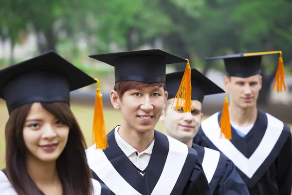 Happy students in graduation gowns on university campus — Stock Photo, Image