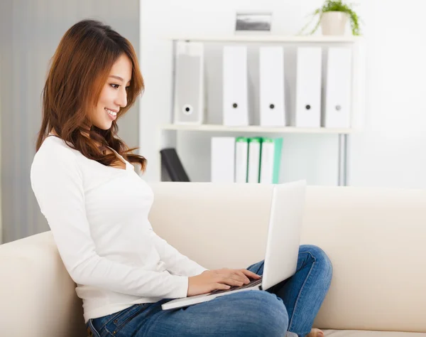 Leende ung kvinna sitter i soffan med laptop — Stockfoto