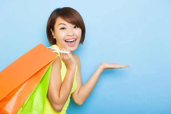 Mujer joven sosteniendo bolsas de compras antes de fondo azul — Foto de Stock