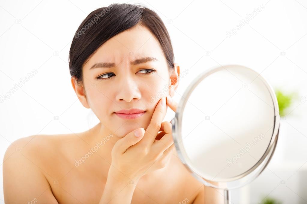  young woman Squeezing pimple looking on mirror