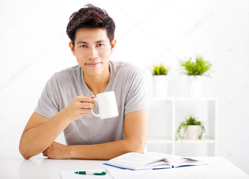 Smiling  young man reading  book  and drinking coffee
