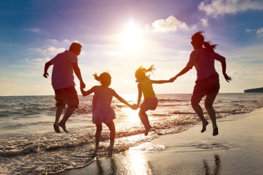 Mutlu bir aile sahilde birlikte zıplıyor.
