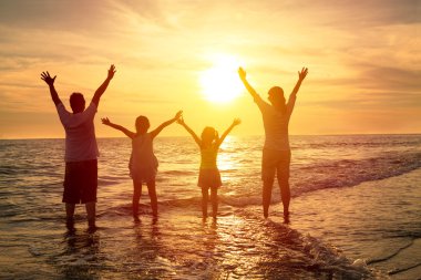 Mutlu bir aile sahilde gün batımını izliyor.