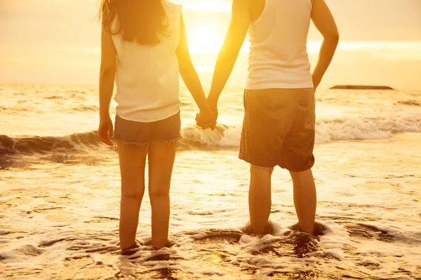 Jovem casal de mãos dadas ao pôr do sol na praia — Fotografia de Stock