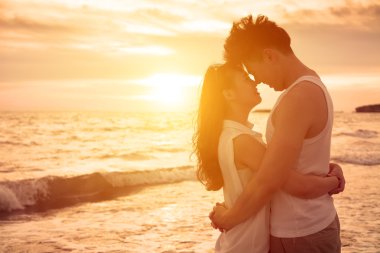 Genç çift gün batımında sahilde öpüşme