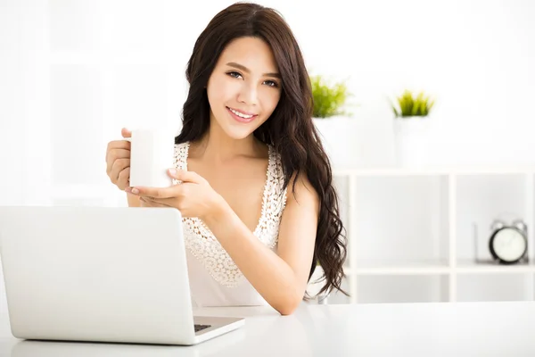 Mujer bonita feliz usando el ordenador portátil y sosteniendo la taza de café —  Fotos de Stock