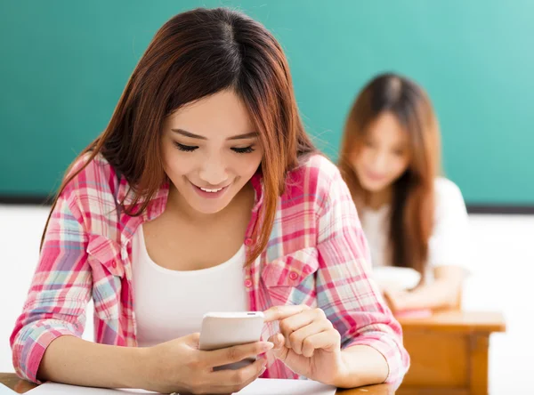 young female student using smart phone in classroom