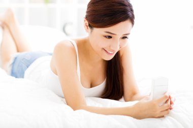 gülümseyen genç kadın yatakta akıllı telefon ile