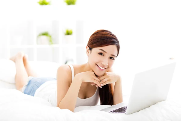 Smiling young woman with laptop on the bed — Stock Photo, Image