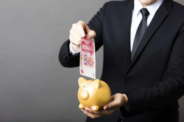 Biznes człowiek oddanie kasy juanów do piggy bank — Zdjęcie stockowe