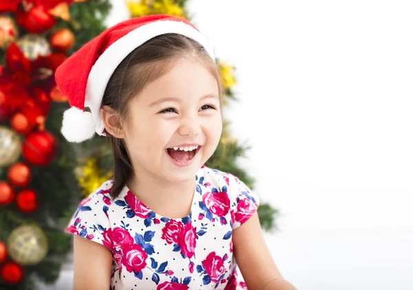 Heureuse petite fille avec chapeau de Père Noël devant l'arbre de Noël — Photo