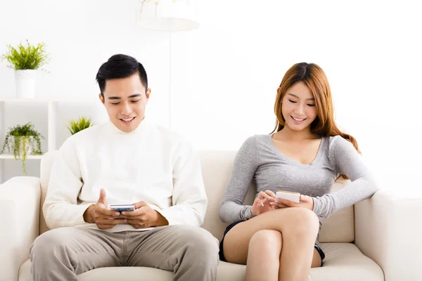 Feliz pareja joven sosteniendo los teléfonos móviles en el sofá —  Fotos de Stock