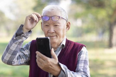 Zavallı görme duyusu. Gözlük takan kıdemli bir adam akıllı telefon kullanıyor.