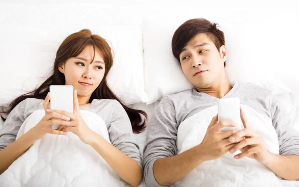 Feliz jovem casal em uma cama com telefones inteligentes — Fotografia de Stock