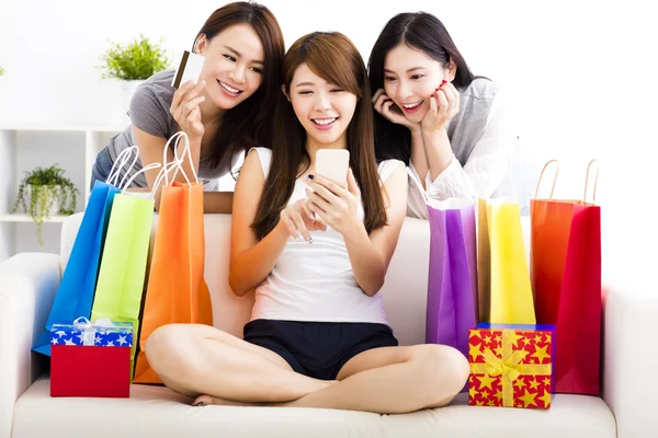 Tres mujeres jóvenes con bolsas de compras y mirando el teléfono inteligente —  Fotos de Stock