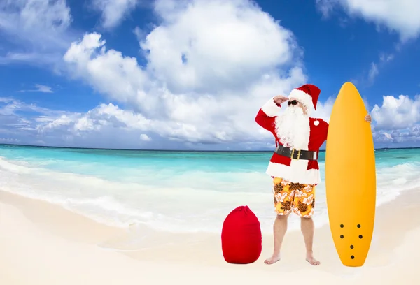 Santa Claus permanent met surfplank op het strand — Stockfoto