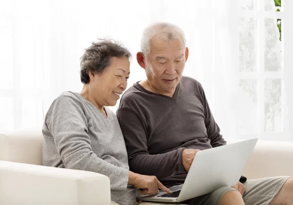 Feliz pareja de ancianos usando el ordenador portátil en el sofá — Foto de Stock