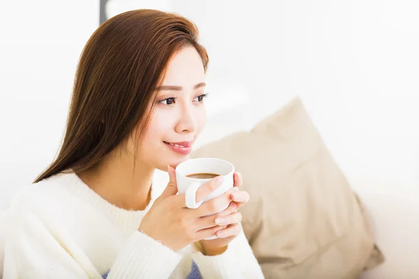 Jovem mulher bebendo café e sentado no sofá — Fotografia de Stock