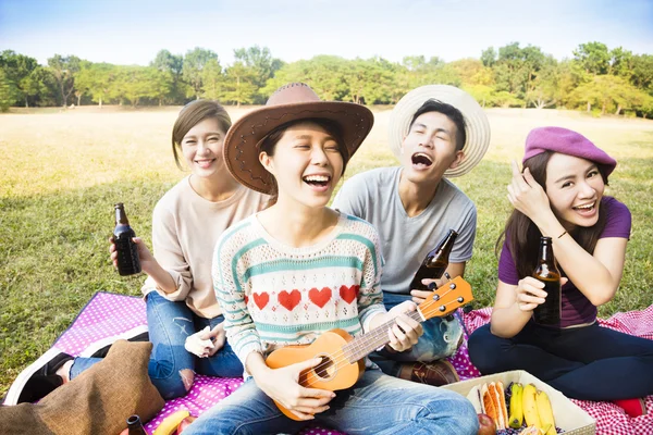 Щасливі молоді друзі насолоджуються пікніком і грають в укулеле — стокове фото