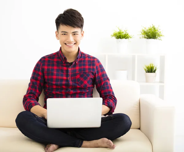 Gelukkig jonge man ontspannen op de Bank met laptop — Stockfoto