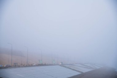Sonbahar şehri manzarası. Şiddetli siste nehir kenarındaki toprak ve şehir yolu.