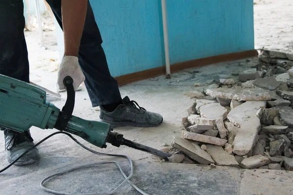Bir işçi tamir odasındaki eski çimento tabakasını çıkarmak için matkap kullanıyor. İnşaat