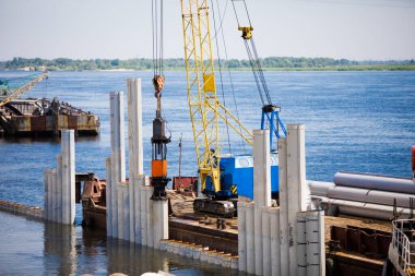 Nehir kıyısında çalışan döşeme makinesi bankayı güçlendirmek ve bir köprü inşa etmek için çekiçleri yığıyor.