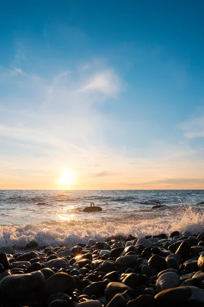Deniz Burnu. Gün batımında vahşi çakıl taşı plajı. Deniz dalgaları kıyıya vuruyor.