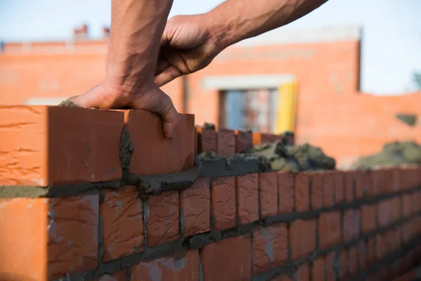 Bricklayer worker installing brick masonry on exterior wall. Professional construction worker laying bricks.