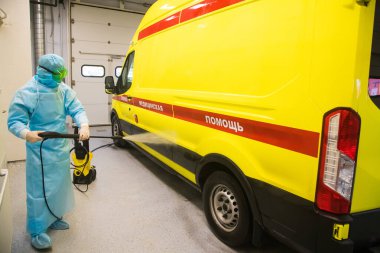 Ambulansın dezenfeksiyonu. Sağlık görevlisi, dezenfektan solüsyonlu ambulansı koronavirüsün yayılmasını önlemek için sprey tabanca ile tedavi eder. Arabanın üzerindeki yazı: resüsitasyon. Acil tıbbi bakım.