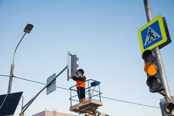 Worker on the lift sets and adjusts the traffic light at the pedestrian crossing. Traffic light and road sign Pedestrian crossing