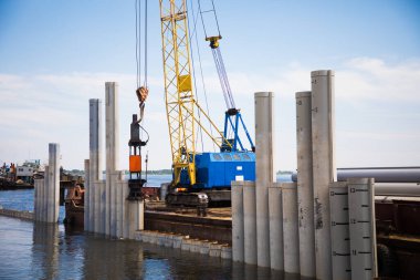 Nehir kıyısında çalışan döşeme makinesi bankayı güçlendirmek ve bir köprü inşa etmek için çekiçleri yığıyor.