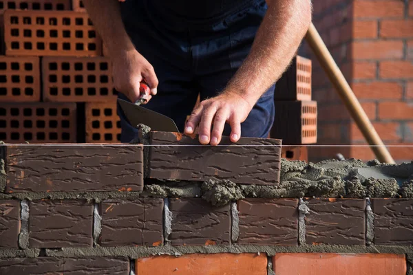 Bricklayer worker installing brick masonry on exterior wall. Professional construction worker laying bricks.