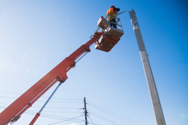 Miğferi ve koruyucu ekipmanı olan işçiler yeni diyot ışıkları kuruyor. Asansör kovası tamir direği işçisi. Sokak lambalarının modernizasyonu. 