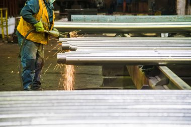 Metal fabrikasında çalışan bir işçi metali öğütür ve keser.