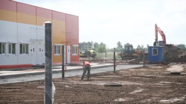 A uniformed worker and construction equipment in the background. Landscaping of the territory near the constructed building. Construction site