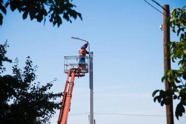 Miğferi ve koruyucu ekipmanı olan işçiler yeni diyot ışıkları kuruyor. Asansör kovası tamir direği işçisi. Sokak lambalarının modernizasyonu. 
