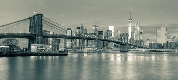 Panoramic view of Brooklyn Bridge and Manhattan skyline in New York City at morning with city illumination, USA. Black and white toned