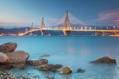 Şehir manzarası - Akşam vakti aydınlatmalı modern köprü. Rion-Antirion Köprüsü, Yunanistan, Avrupa. Yunanistan 'daki Rion-Antirion Köprüsü dünyanın en uzun kablo destekli köprülerinden biri ve tamamen askıya alınmış B tipi köprülerin en uzunu.