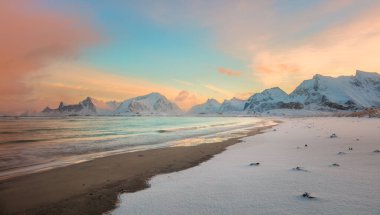 Deniz kıyısında ve dağların üzerinde kış günbatımı, pembe bulutların içinde renkli kuzey gündoğumu ve güneş ışığı. Lofoten Adaları, Norveç, Avrupa