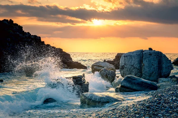 汹涌的海浪冲击着海滩上的岩石 海水在阳光下飞溅而上 日落在海上 专注于前景 — 图库照片