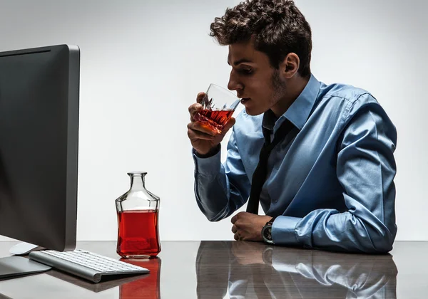Young alcoholic man drinking whiskey sitting drunk at office with computer