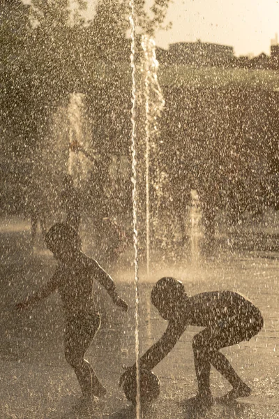 Silhouette of a kid playing in a sunny water fountain — Stock Photo, Image