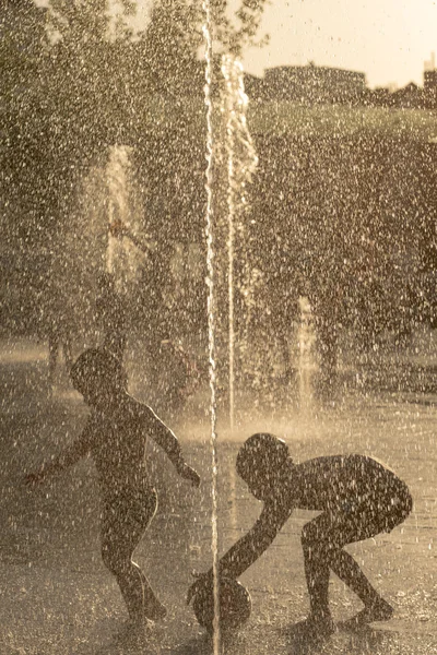 Silhouette di un bambino che gioca in una fontana soleggiata — Foto Stock