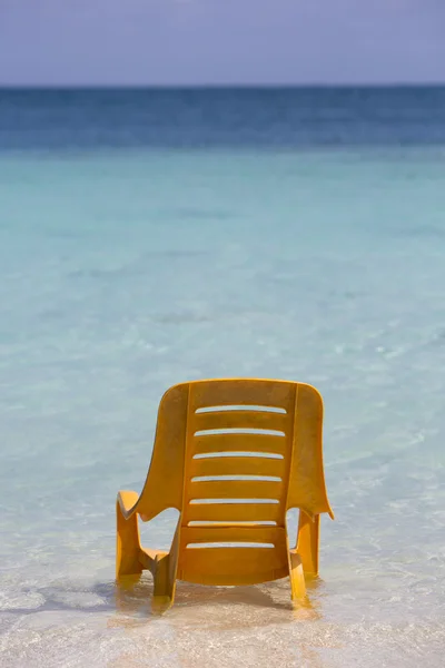 Een oranje plastic stoel staande in het water op tropisch strand — Stockfoto