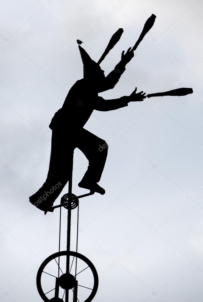 Silhouette of clown juggling and riding unicycle with bird