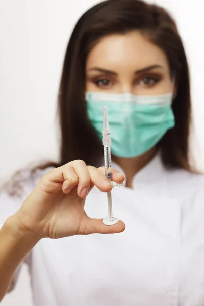 woman doctor shows syringe, shallow depth woman is out of focus and syringe is in focus
