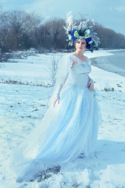 Mavi elbiseli ve çiçekli taçlı bir kış perisi.