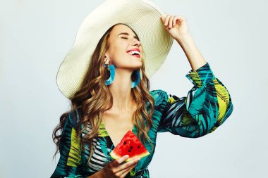 Güzel bir kadın şapkası ve elinde karpuz tutan yeşil bir elbiseyle gülümsüyor.