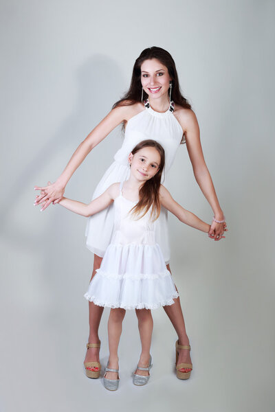 Mother and daughter in same outfits posing on studio on bright background